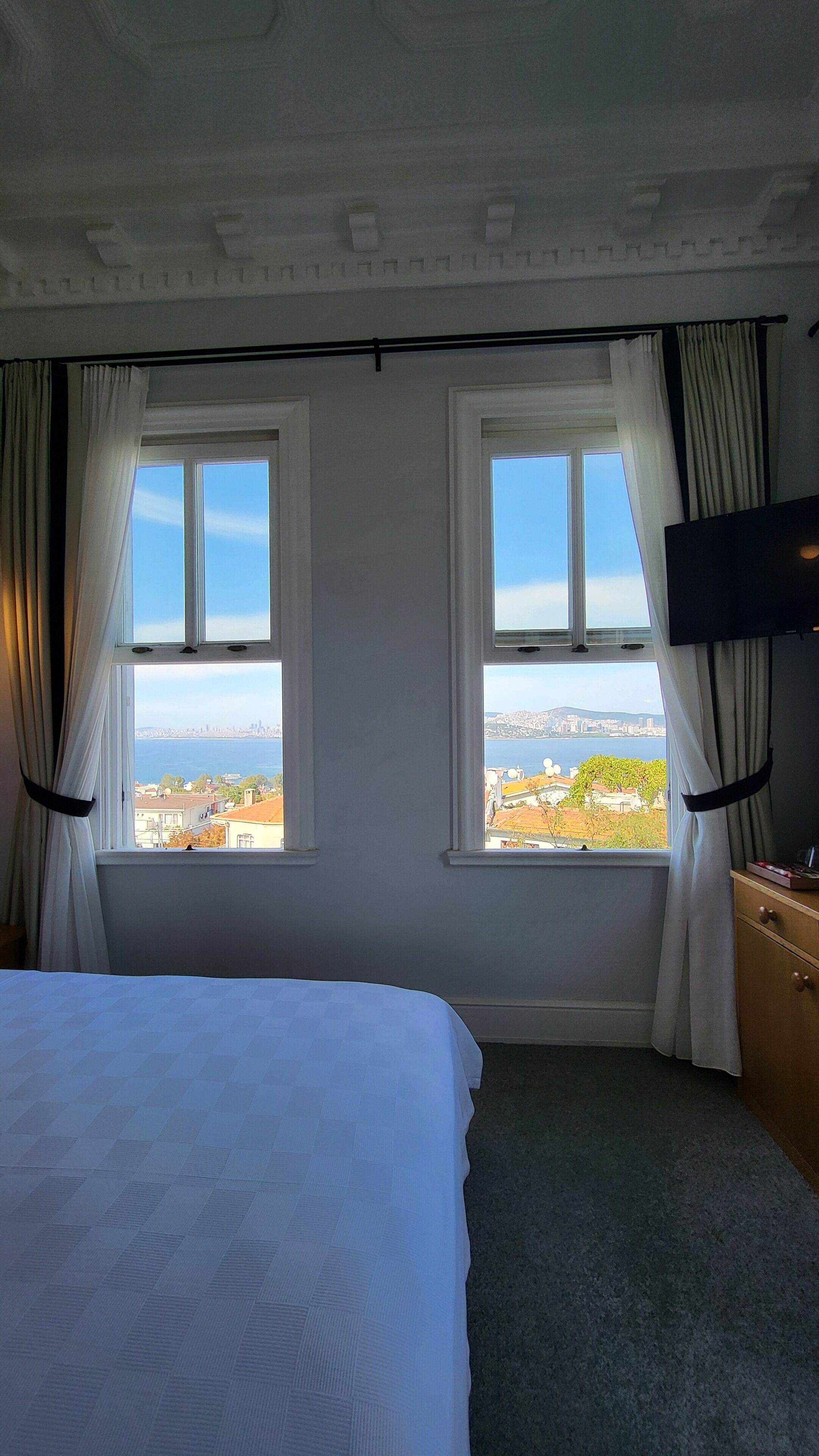 Una habitación de hotel con dos ventanas, una cama, un televisor y un aparador de madera.