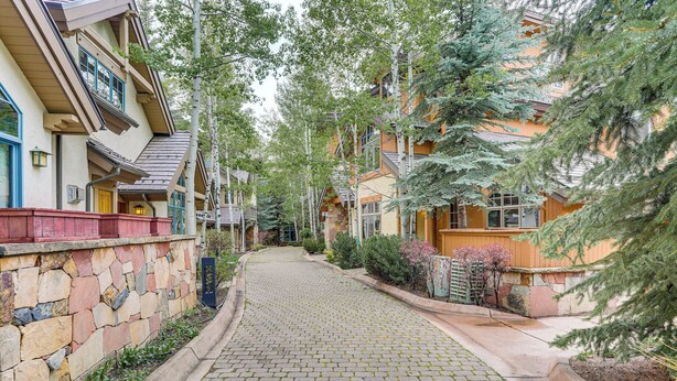 A cobblestone street flanked by multi-story buildings with stone walls and wooden railings, surrounded by trees and shrubs. - Walk to Lift: Arrowhead Ski Condo w/ Pool Access! (Edwards)