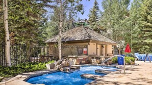 A pool area with a hot tub, a wooden deck, and a stone wall. - Walk to Lift: Arrowhead Ski Condo w/ Pool Access! (Edwards)