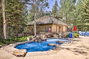 A pool area with a hot tub, a wooden deck, and a stone wall.