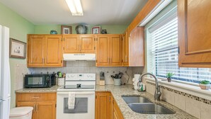 A kitchen with wooden cabinets, a microwave, stove, sink, and a window with blinds. - Convenient St Simons Island Home - 3 Mi to Beach! (St. Simons Island)