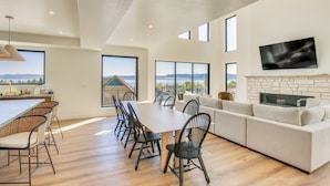 A spacious living room with a large sofa, dining table, and chairs, a fireplace, and a TV mounted on the wall. - Luxe Retreat w/ Theater Room: Walk to Bear Lake! (Garden City)