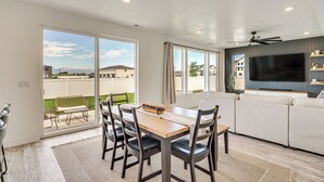 Una sala de estar moderna con un televisor grande, un sofá y un comedor con sillas y una mesa.