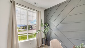 Una habitación moderna con un ventanal grande, una planta en maceta, un sillón color beige y una mesita de madera.