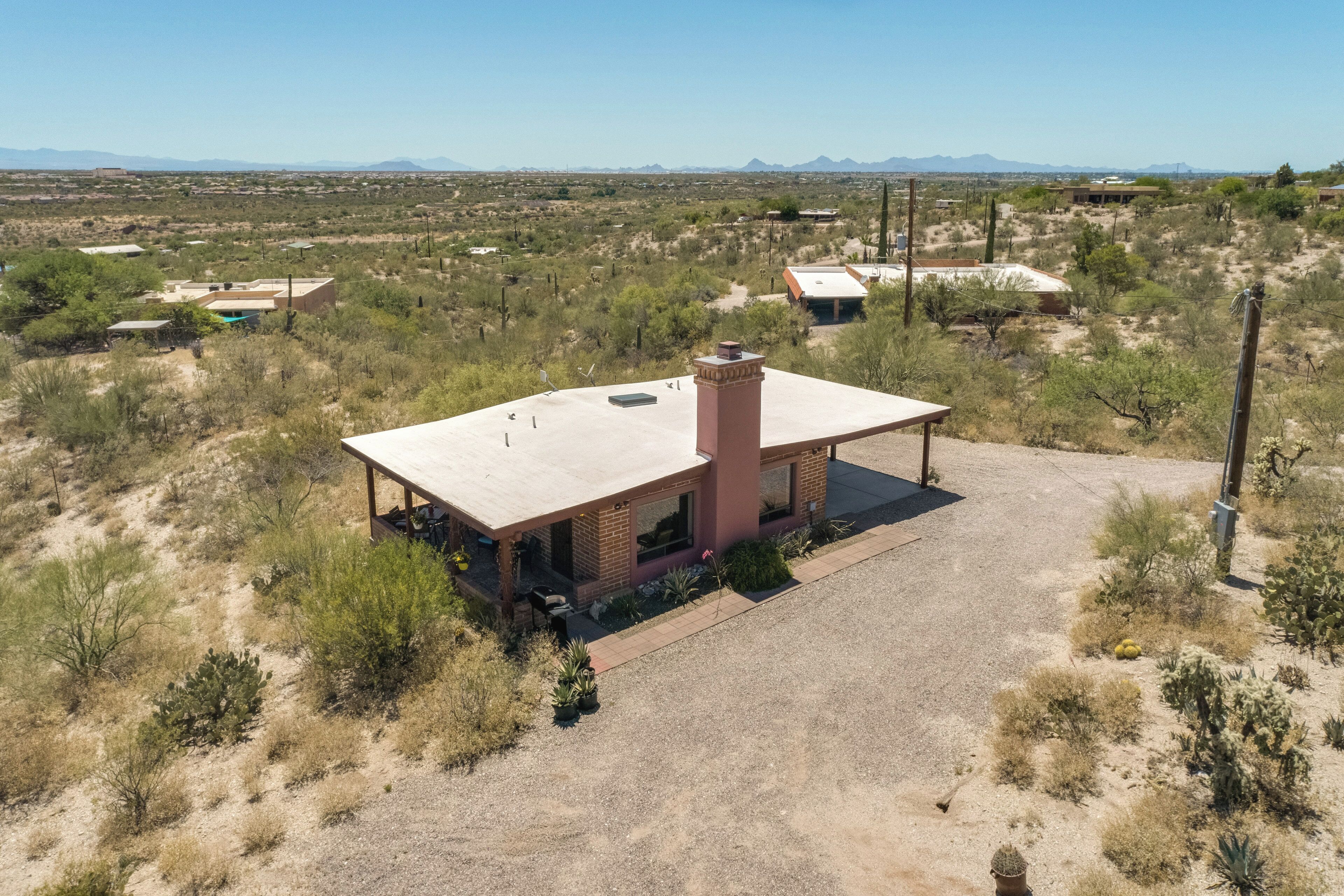 A single-story building with a flat roof and a chimney, surrounded by desert vegetation and distant mountains.