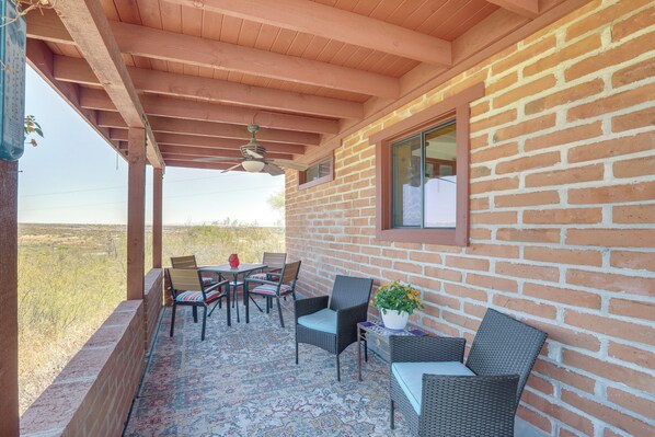A covered patio with a brick wall, a ceiling fan, and outdoor furniture including chairs and a table. - Near Hiking: Mtn-view Tucson Studio Retreat (Tucson)