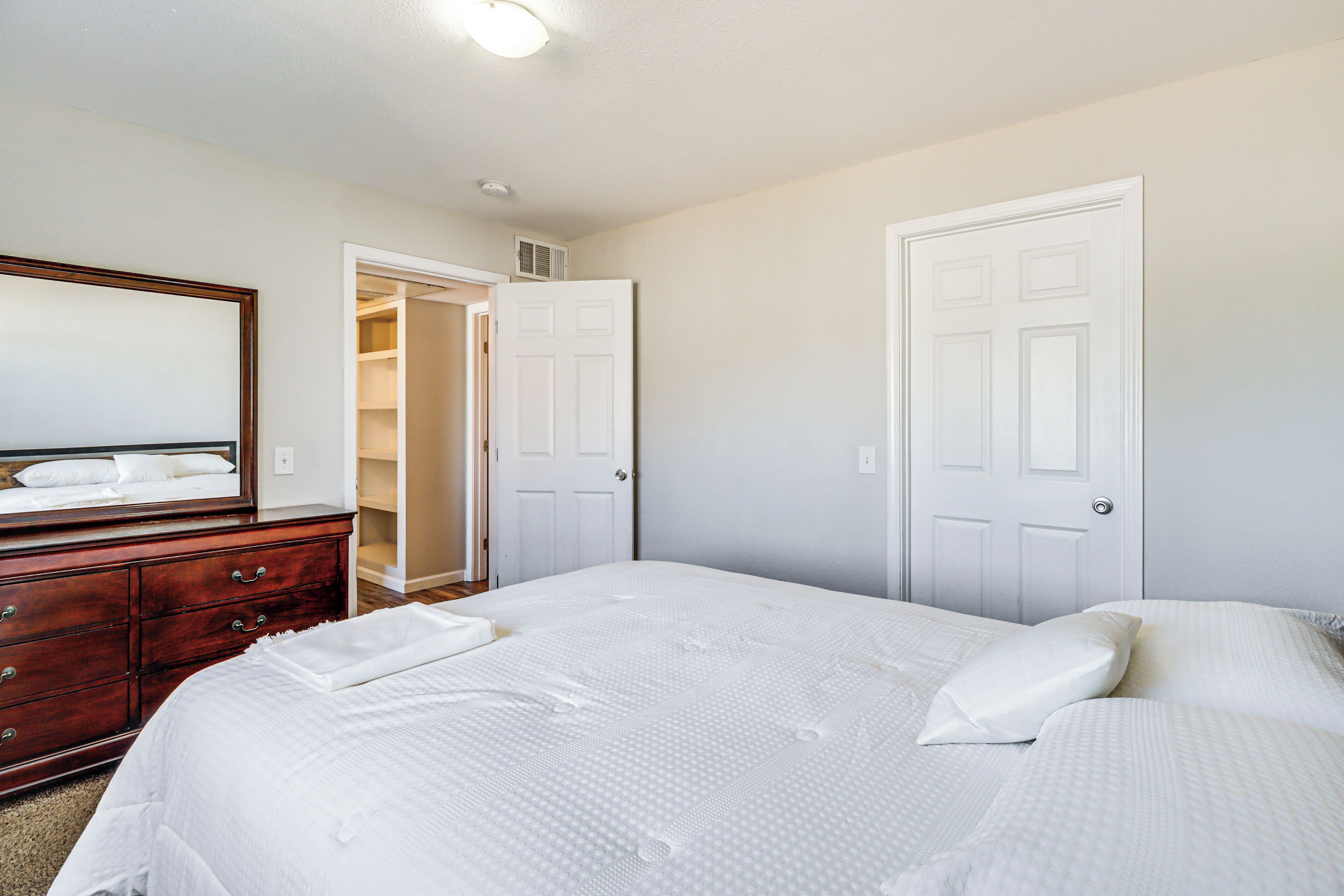 A bedroom with a large bed, a dresser, and a walk-in closet.