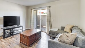 Un salon avec un téléviseur à écran plat posé sur un meuble en bois, un canapé gris agrémenté de coussins à motifs et une table basse en bois.