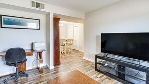 Un salon avec un téléviseur à écran plat, une table basse en bois, un fauteuil de bureau noir et un tableau encadré accroché au mur.