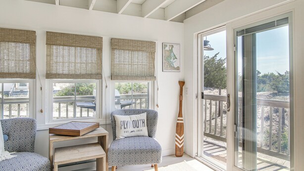 A room with a large sliding glass door leading to a balcony, patterned chairs, a wooden table, and a map on the wall. - Steps to the Sand! Plymouth Beach Cottage (Plymouth)
