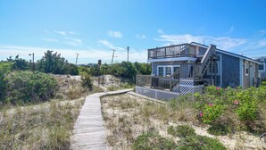 A coastal house with a wooden deck, a staircase leading to a balcony, and a sandy path. - Steps to the Sand! Plymouth Beach Cottage (Plymouth)