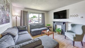 A living room with a gray sofa, a wooden coffee table, a gray armchair, a flat-screen TV mounted on the wall, and a window with curtains. - Family-friendly Clovis Home w/ Gas Grill + Patio! (Clovis)