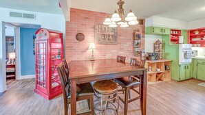 A dining area with a wooden table and chairs, a red telephone booth, and a green kitchen area with cabinets and shelves. - Family-friendly Clovis Home w/ Gas Grill + Patio! (Clovis)