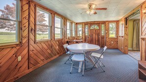 Una habitación con paredes de madera, ventanas amplias, un ventilador de techo y una mesa redonda con sillas.
