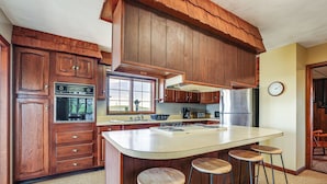 Una cocina con armarios de madera, una isla grande con taburetes y un refrigerador de acero inoxidable.