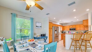 A modern kitchen with wooden cabinets, a central island, and a dining area with blue chairs and a table set for four. - 4 Mi to Rainbow Springs: Dunnellon Home w/ Pool! (Dunnellon)