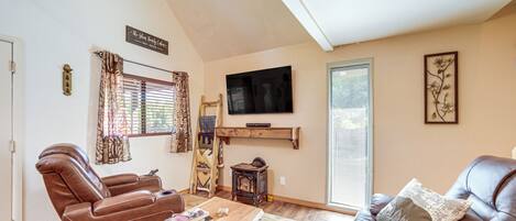 A living room with a brown leather sofa, a wooden coffee table, a TV mounted on the wall, and a window with blinds.