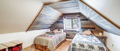 A cozy attic bedroom with two wooden beds, a small table, and a bench.