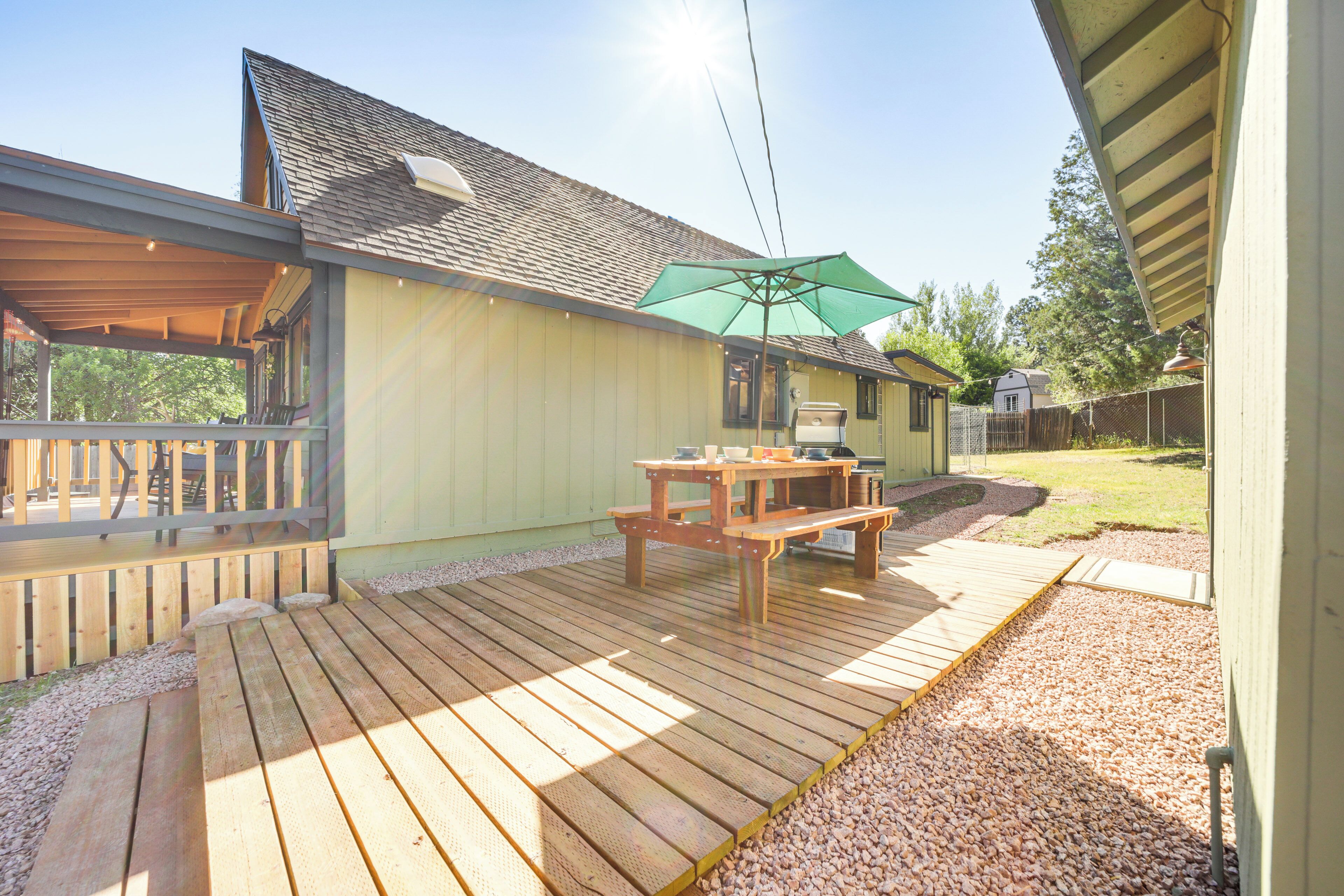 A wooden deck with a picnic table and umbrella, surrounded by a gravel area and a wooden fence.