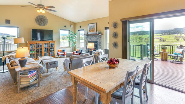 A spacious living room with a wooden dining table, comfortable seating, a fireplace, and a large window offering a view of the outdoors. - Spearfish Retreat w/ Fireplace + Mountain Views! (Spearfish)