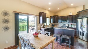 A kitchen with dark cabinets, a stainless steel refrigerator, and a dining area with a wooden table and white chairs. - Spearfish Retreat w/ Fireplace + Mountain Views! (Spearfish)