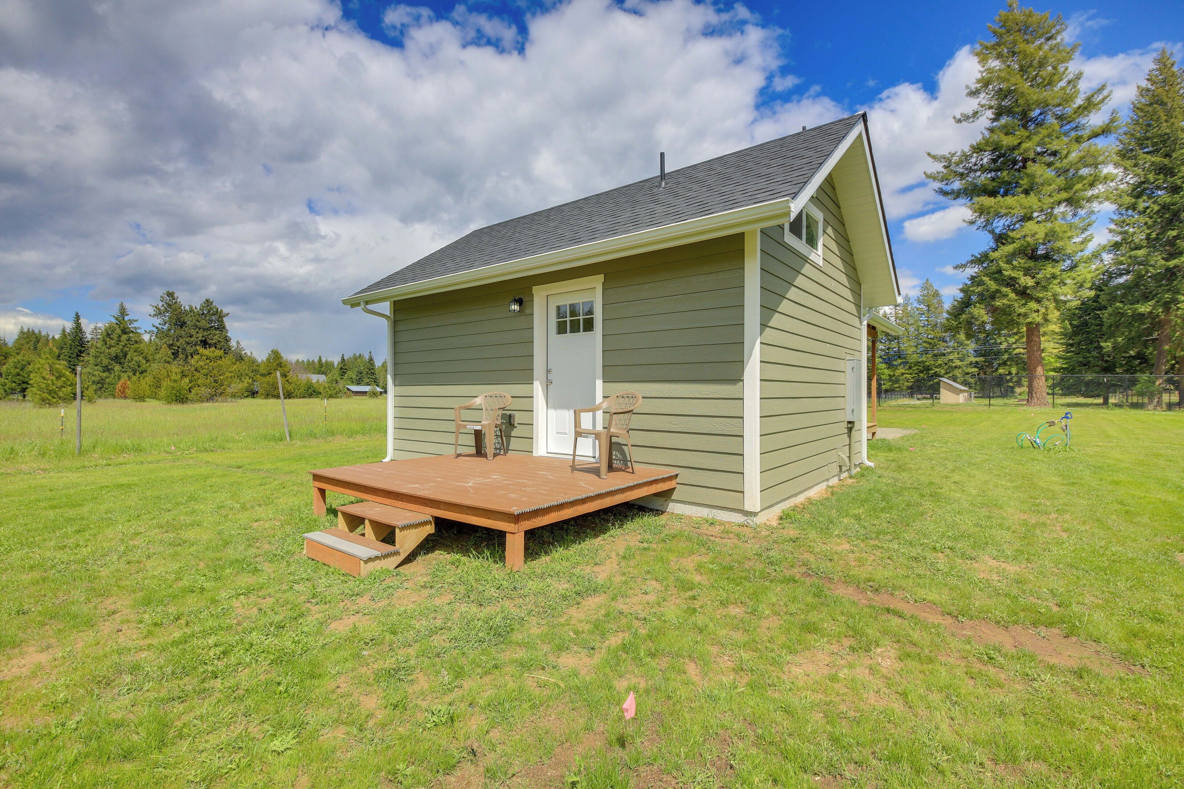 A small, single-story house with a front porch and a deck, surrounded by a grassy yard and trees.