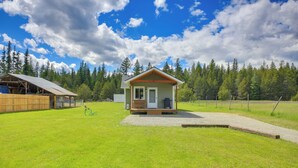 Une petite cabane dotée d’une terrasse en bois, entourée d’une cour verdoyante et d’une forêt.