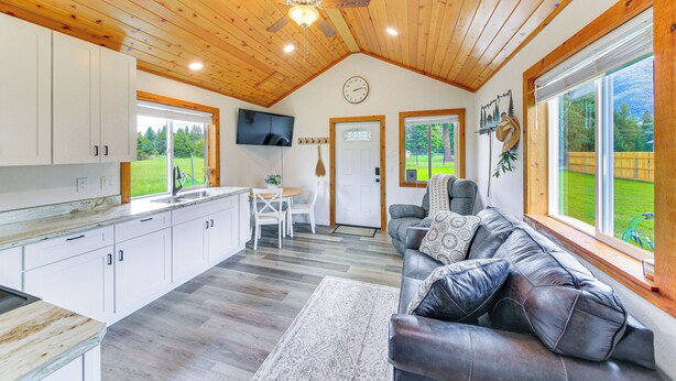Une cuisine spacieuse avec des meubles blancs, un coin repas comprenant une table et des chaises, un canapé en cuir et de grandes fenêtres offrant une vue sur l’extérieur.