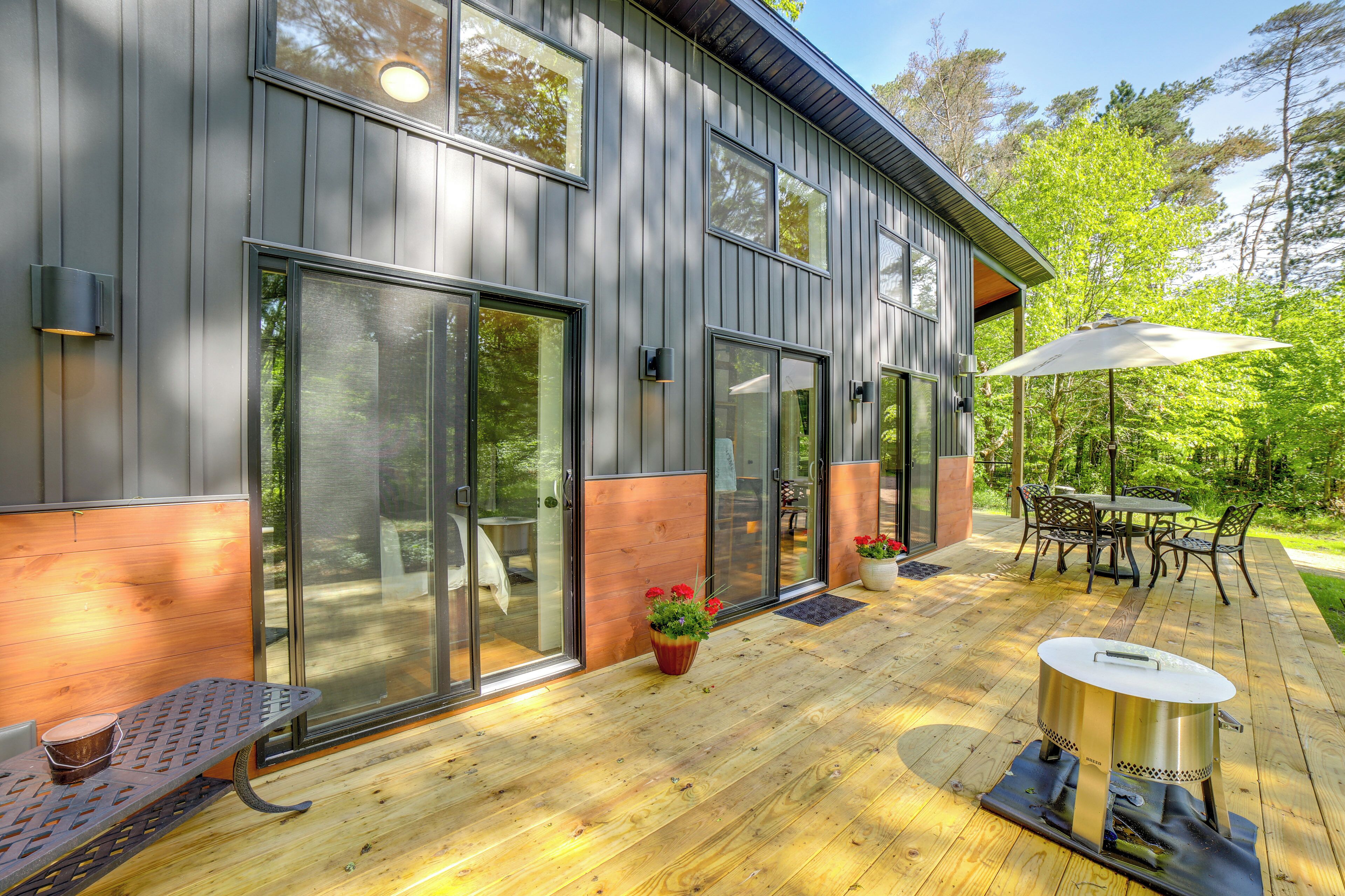 A modern house with large sliding glass doors, a deck with outdoor furniture, and a barbecue grill.