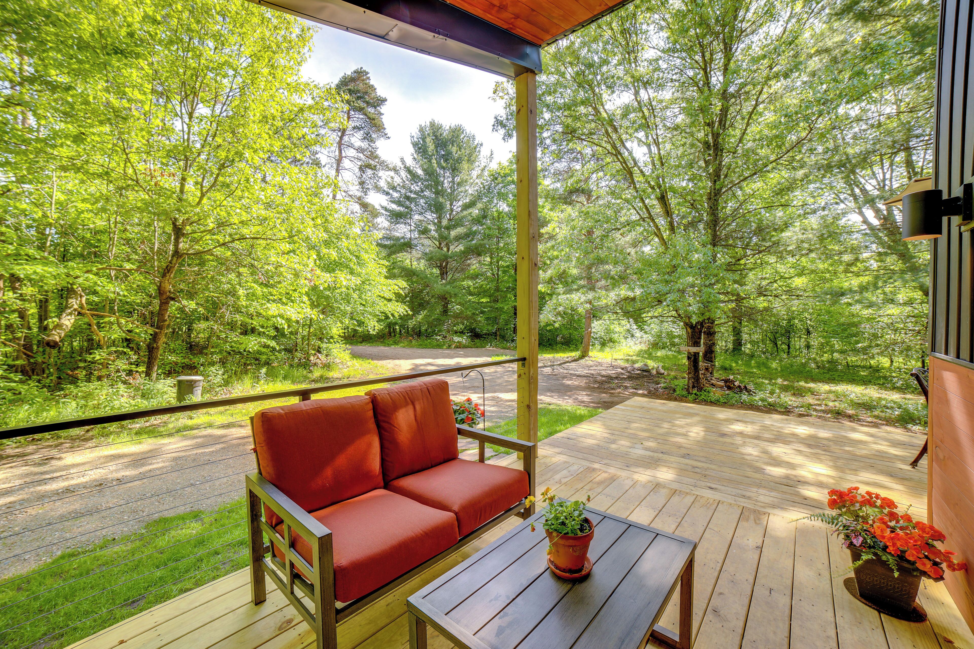 A wooden deck with a red sofa and a table, surrounded by greenery and trees.