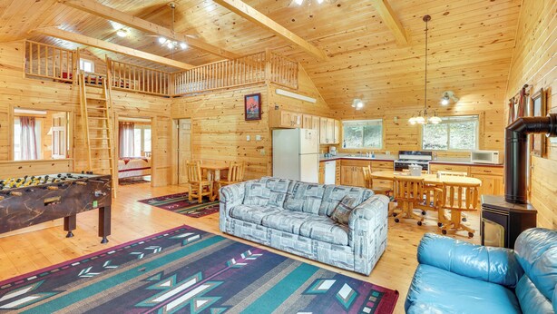 A spacious wooden cabin with a loft bedroom, a dining area, a kitchen, and a living room with a sofa and a foosball table. - Wraparound Deck & Grill: Deadwood Cabin (Deadwood)