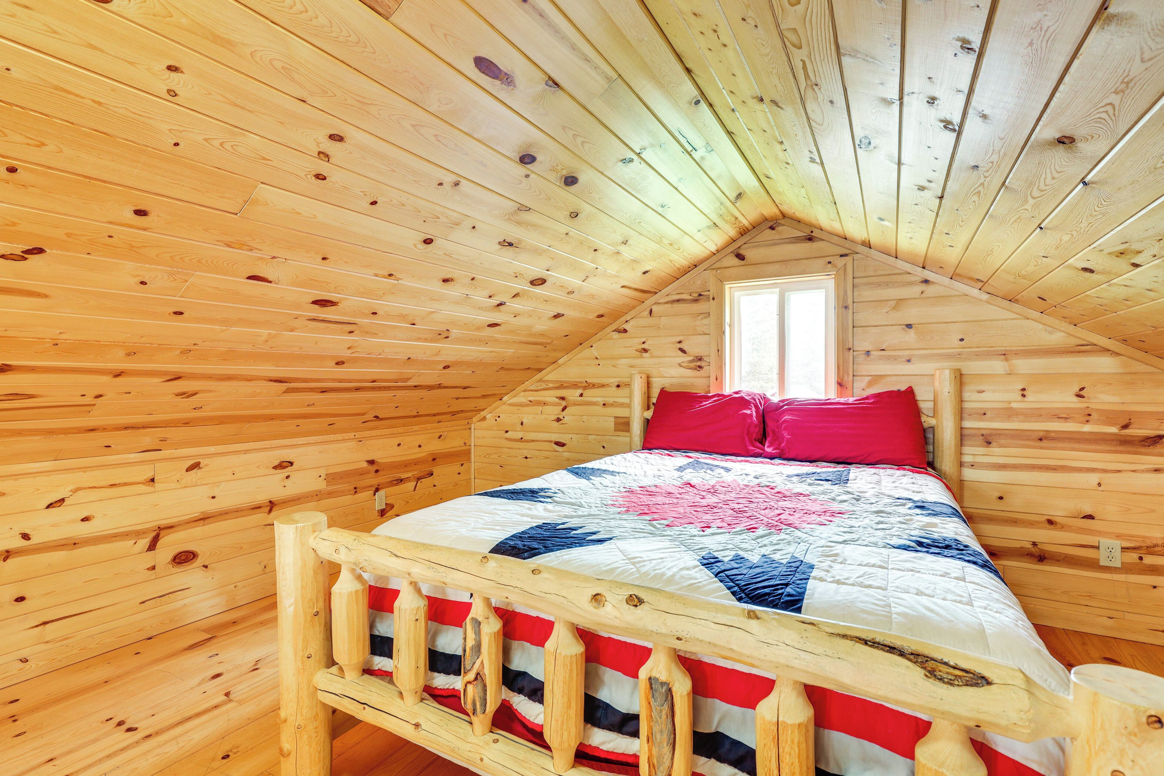 A wooden cabin room with a bed, a window, and a sloped ceiling.