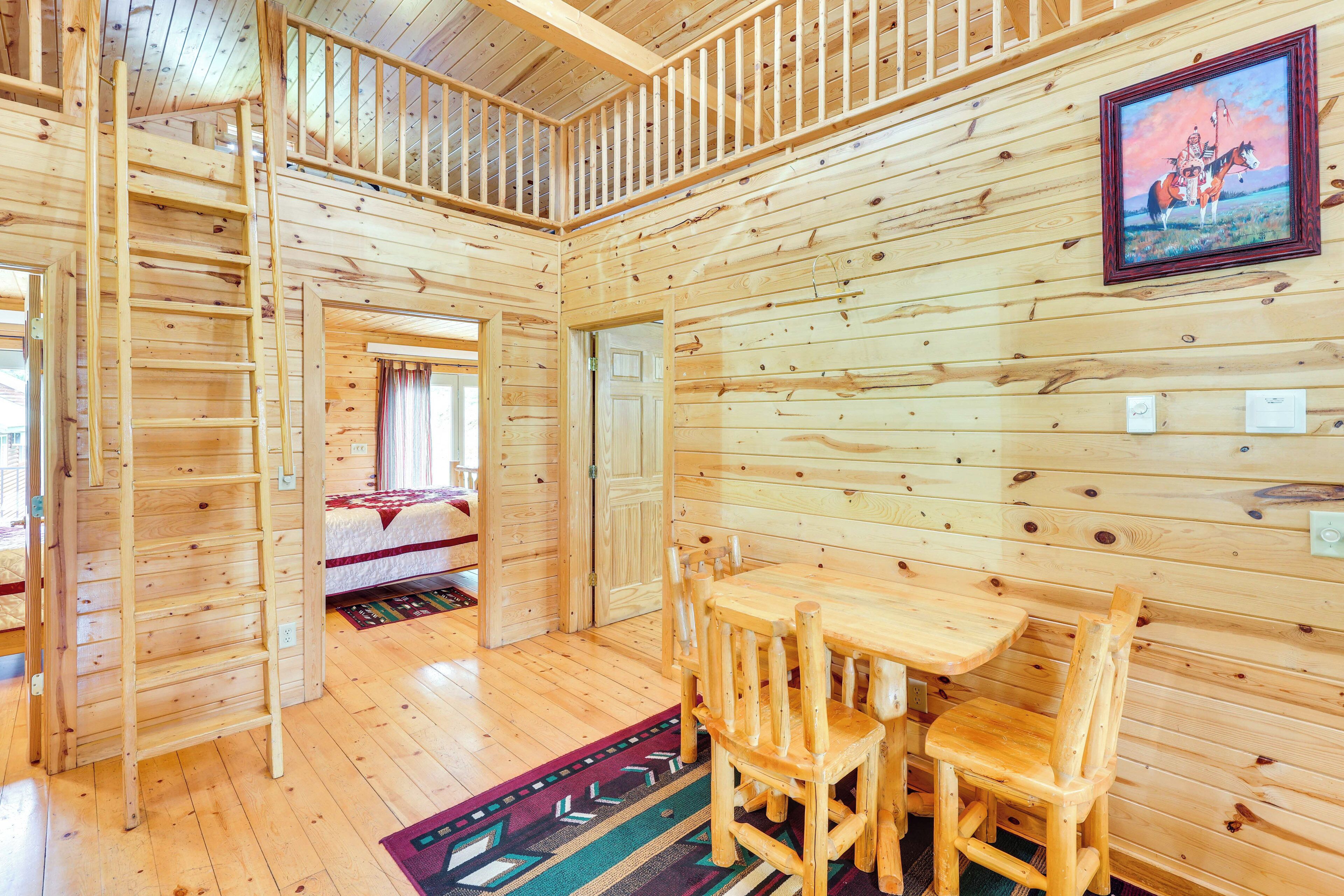 A wooden cabin interior with a dining area, a bed, and a staircase.