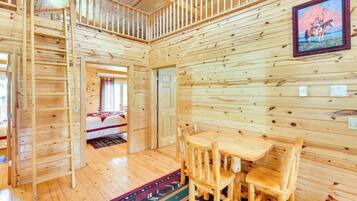 A wooden cabin interior with a dining area, a bed, and a staircase.