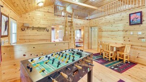 A wooden interior with a foosball table, a balcony, and a dining area with chairs. - Wraparound Deck & Grill: Deadwood Cabin (Deadwood)