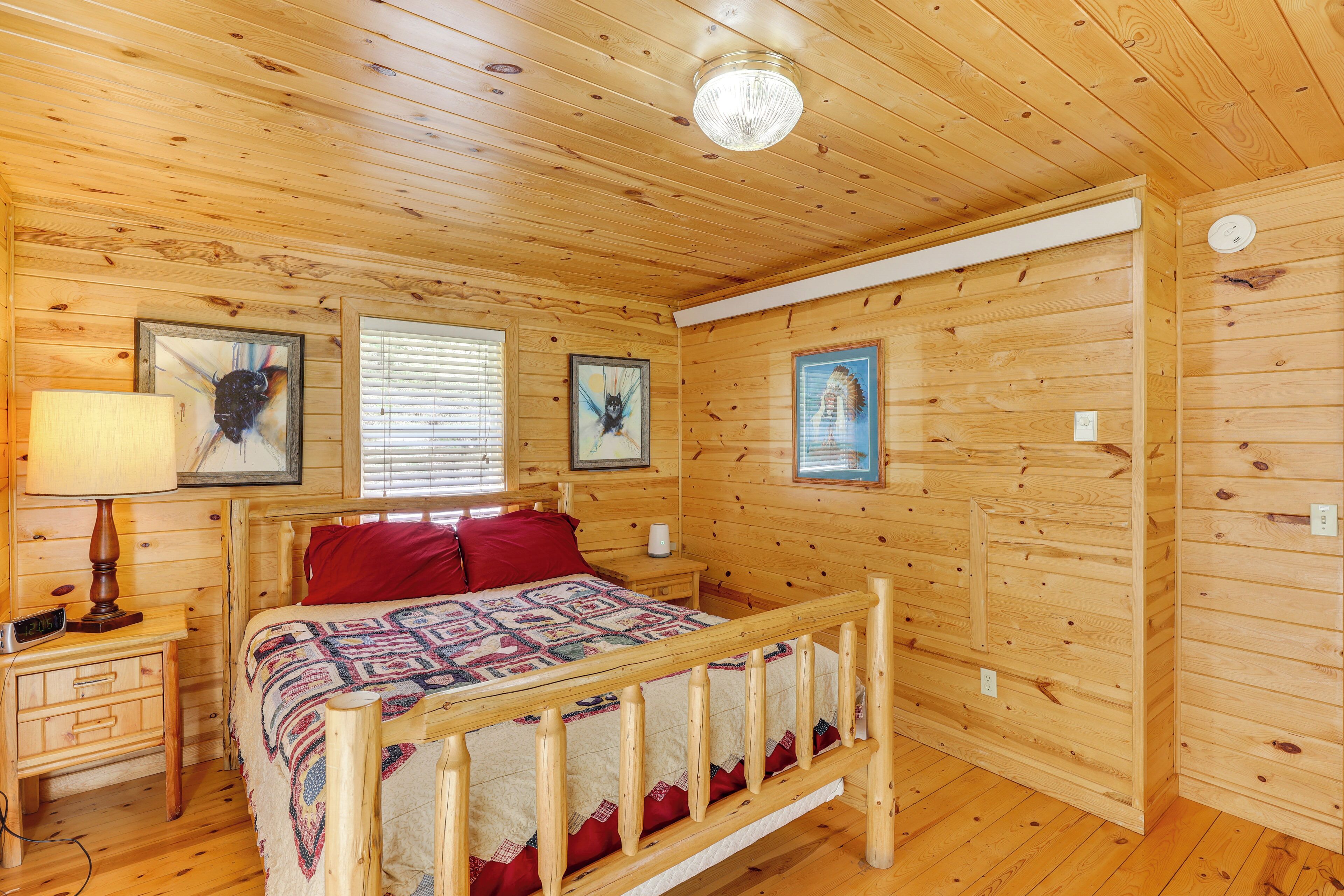 A wooden-paneled bedroom with a bed, nightstands, and artwork on the walls.