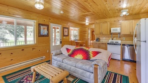 A cozy cabin interior with a wooden ceiling, a sofa with a colorful quilt, a dining area, and a kitchen with modern appliances. - Pets Welcome: Cozy Cabin w/ Deck in Deadwood! (Deadwood)