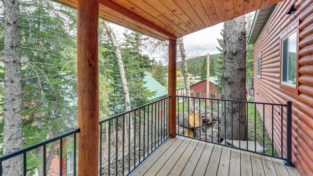 A wooden deck with a railing, surrounded by trees and a log cabin. - Hike, Unwind & Bring Your Pet: Deadwood Cabin! (Deadwood)