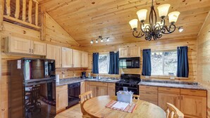 Une cuisine rustique aménagée dans une cabane en bois, comprenant un réfrigérateur, une cuisinière, un four à micro-ondes et des placards en bois.