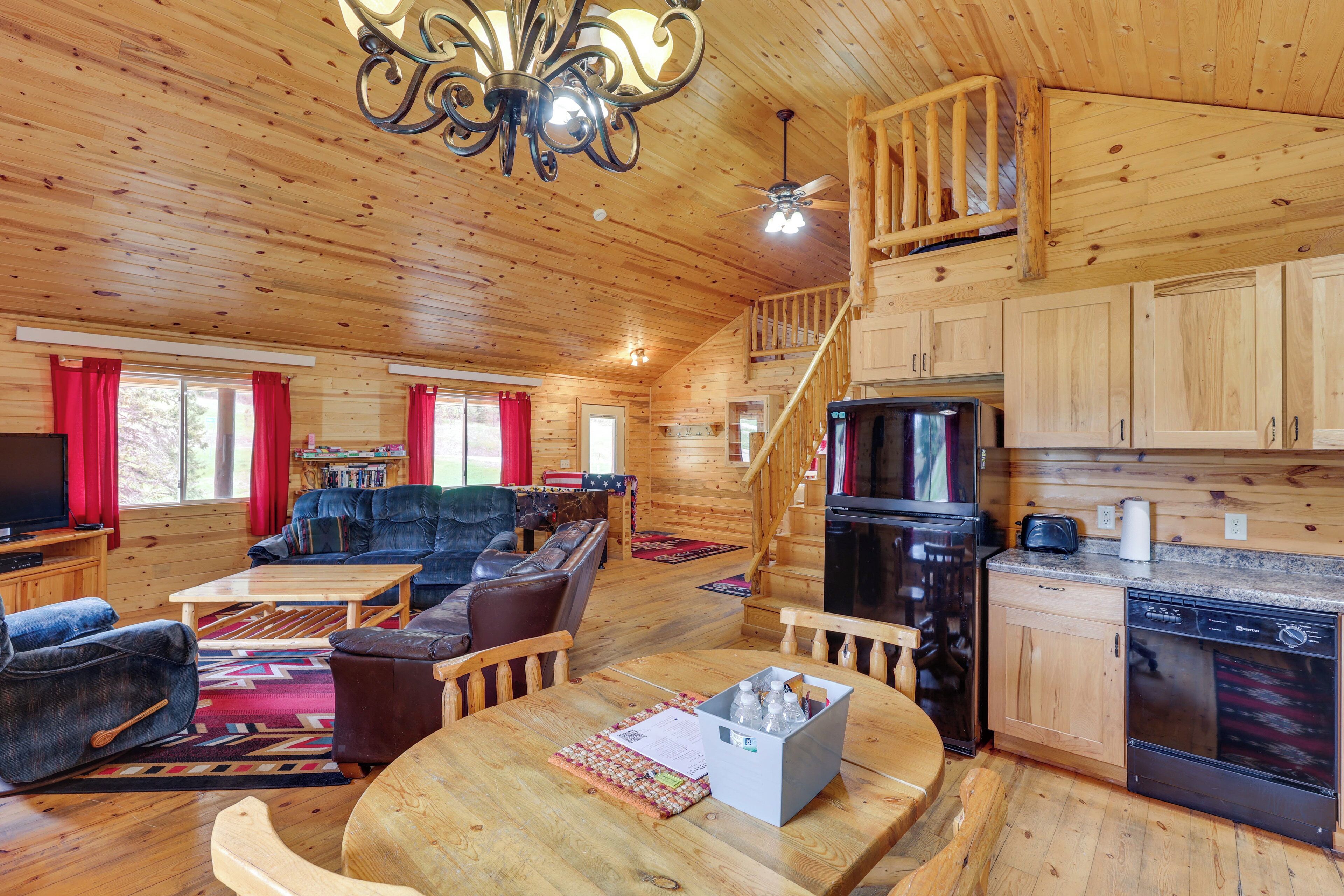 A wooden cabin interior with a living room, dining area, kitchen, and a staircase.