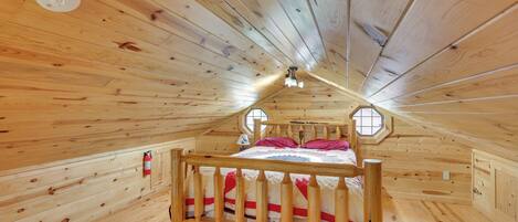 A wooden cabin room with a bed, a window, and a ceiling light.