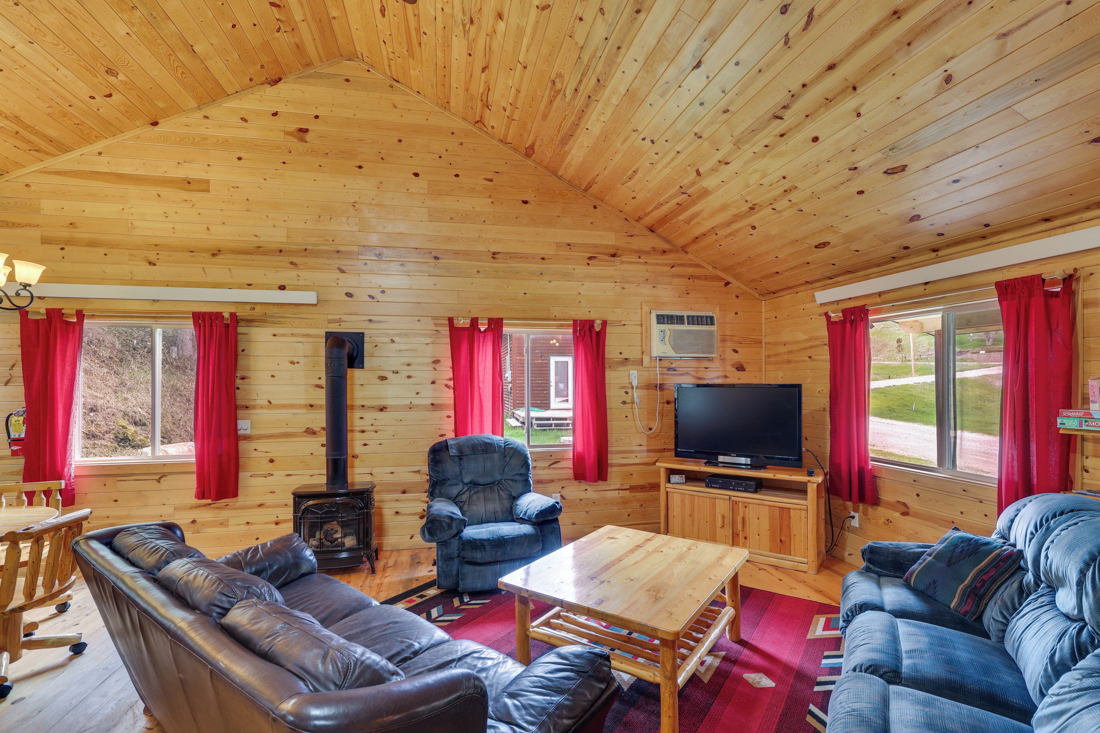 A cozy cabin interior with a wooden ceiling, a sofa, a chair, a table, a television, and a fireplace.