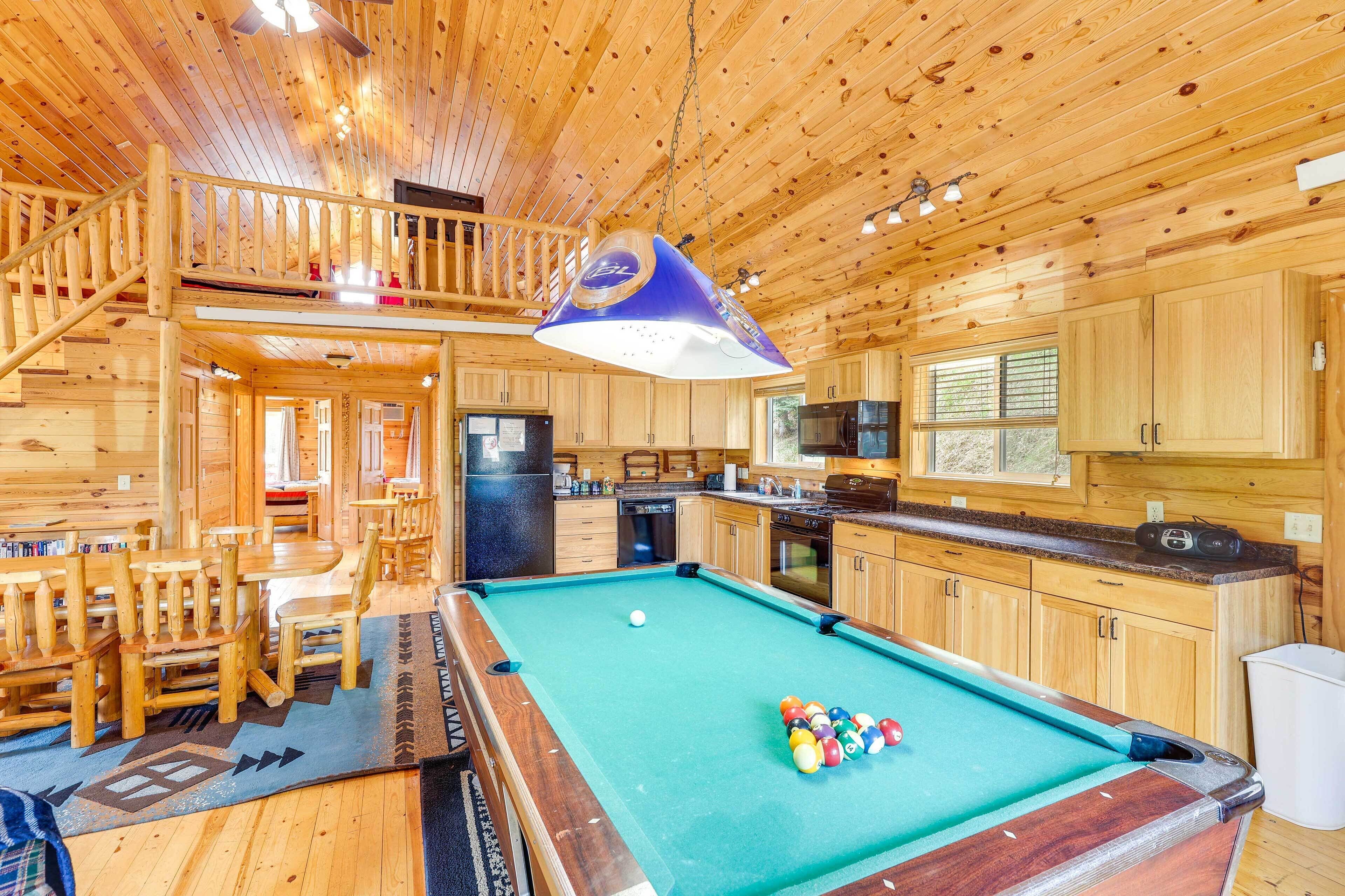 L’intérieur d’un chalet en bois comprend une table de billard, un coin repas, une cuisine et un balcon.