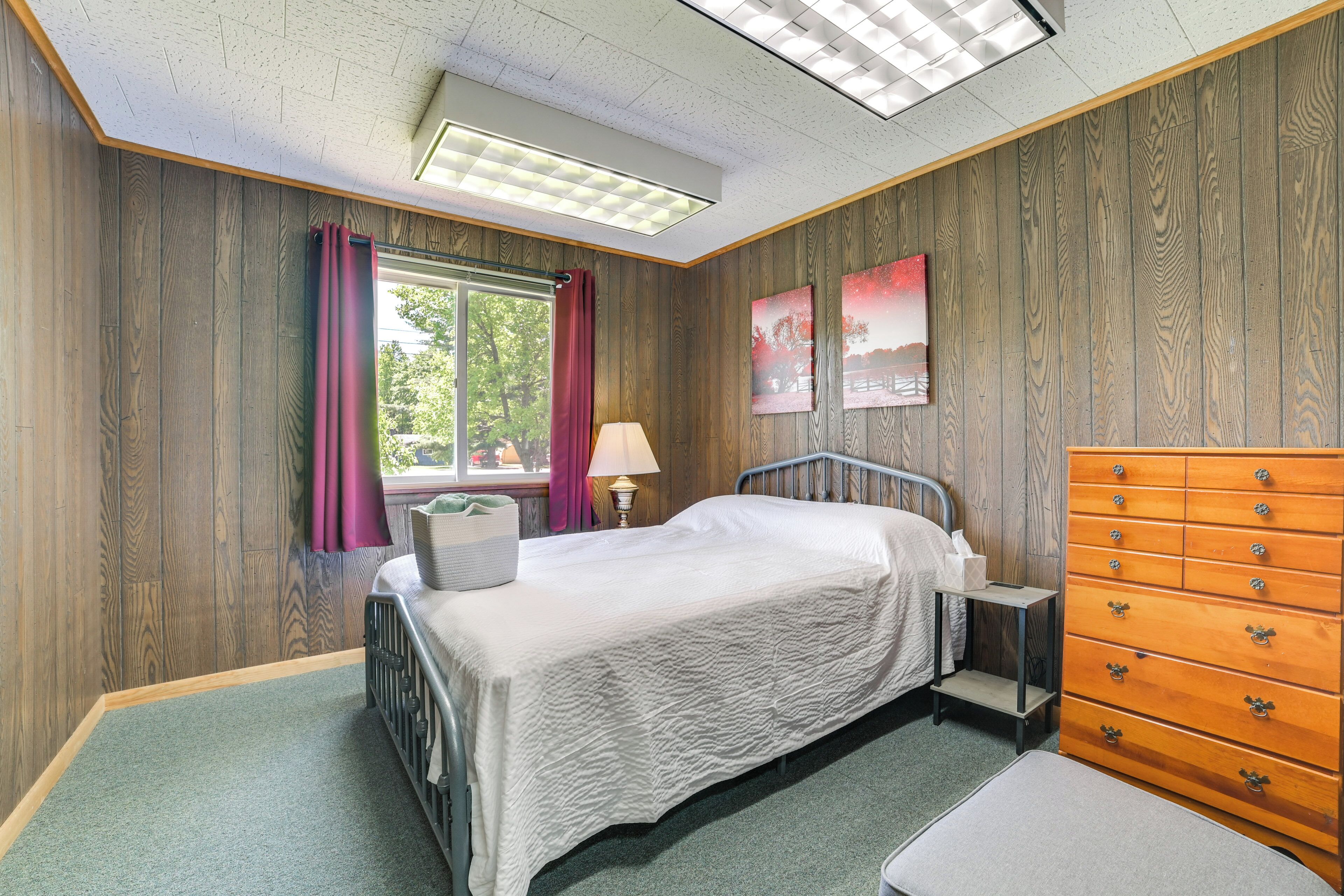 A bedroom with a bed, dresser, lamp, and window with curtains.