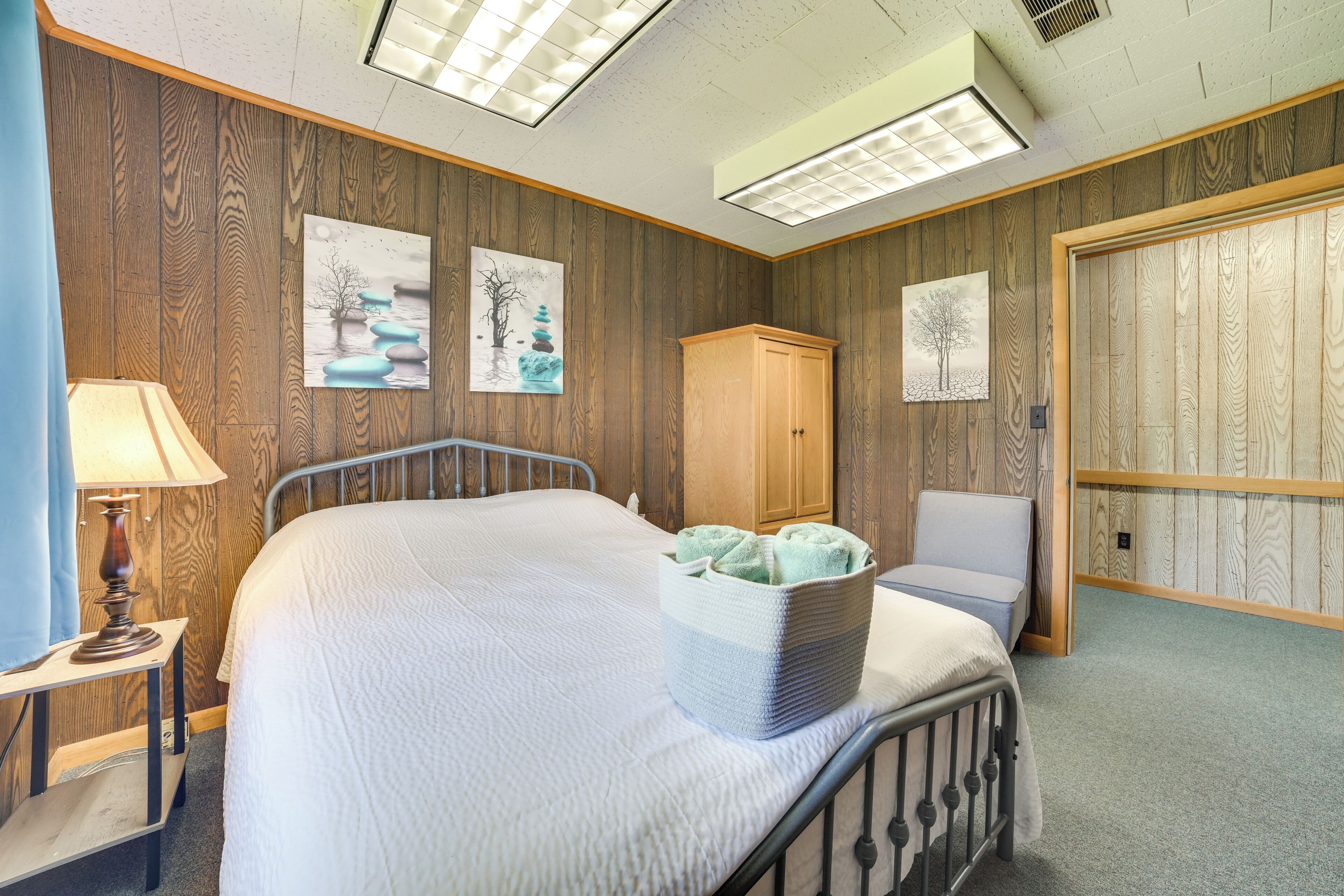 A bedroom with a bed, a nightstand, a lamp, a cabinet, and artwork on the walls.