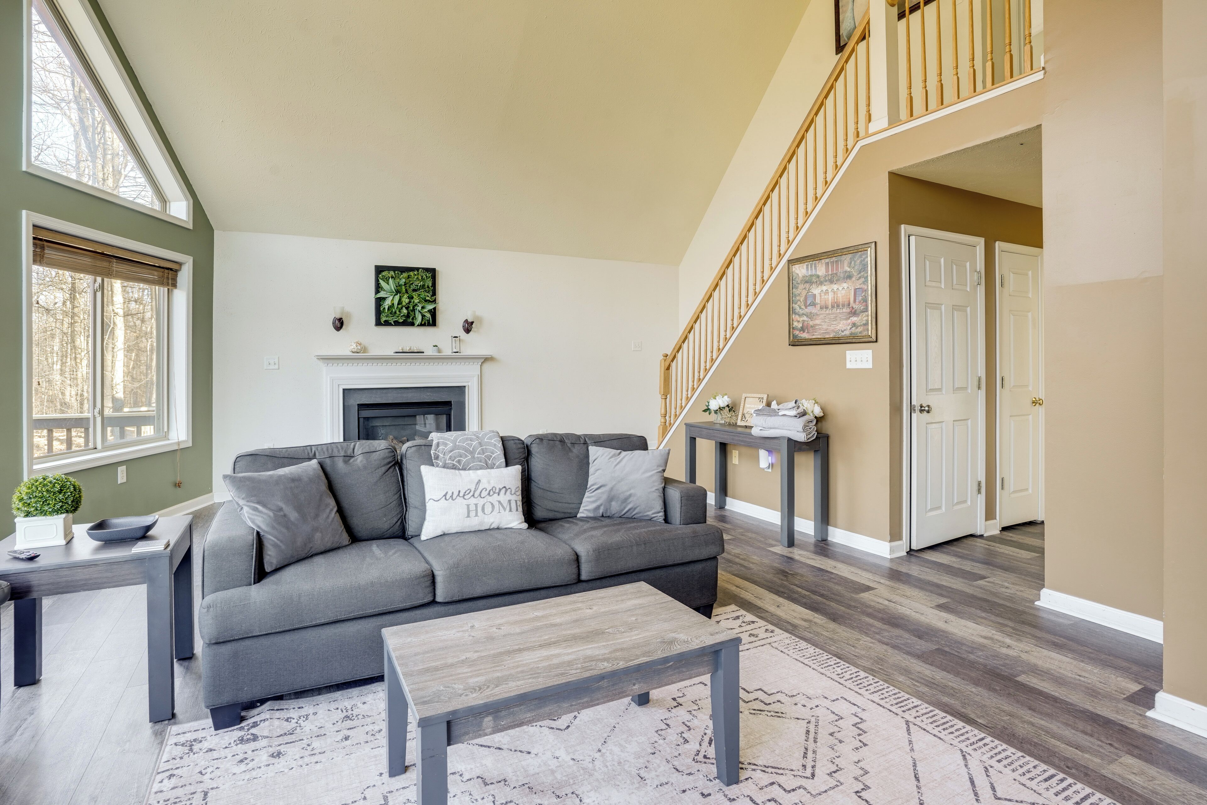 A living room with a gray sofa, a fireplace, a staircase, and a view of the outdoors.