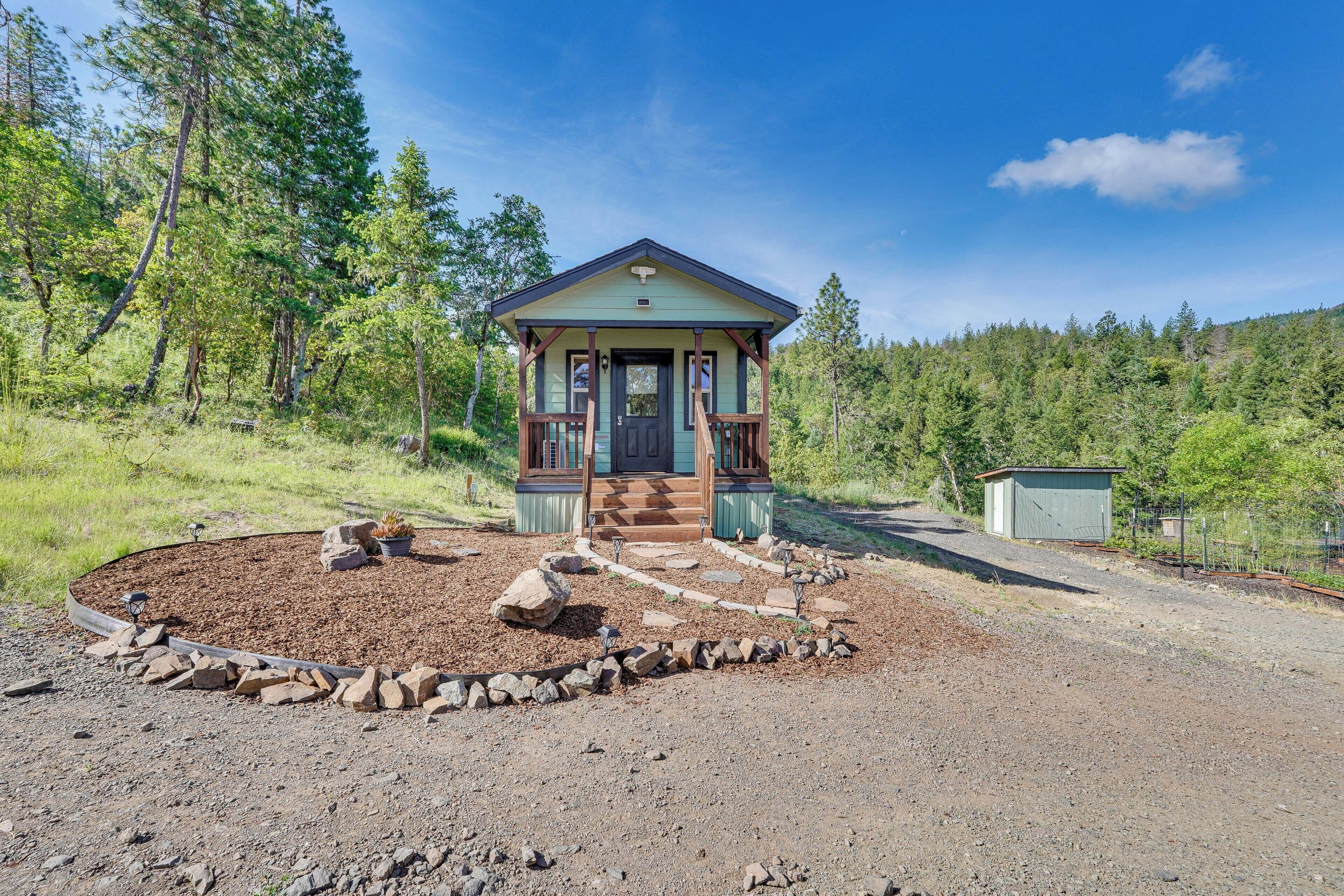 A small cabin with a porch, surrounded by a landscaped garden with rocks and mulch.