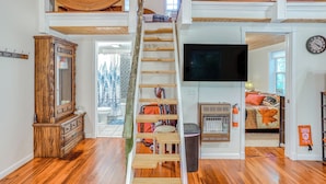 A spacious living area with a wooden staircase, a large flat-screen TV, and a fireplace. - Secluded Vacation Rental Bordering Creek! (Mountain View)