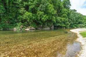 A clear river with visible rocks and a sandy bank, surrounded by dense green foliage. - Secluded Vacation Rental Bordering Creek! (Mountain View)