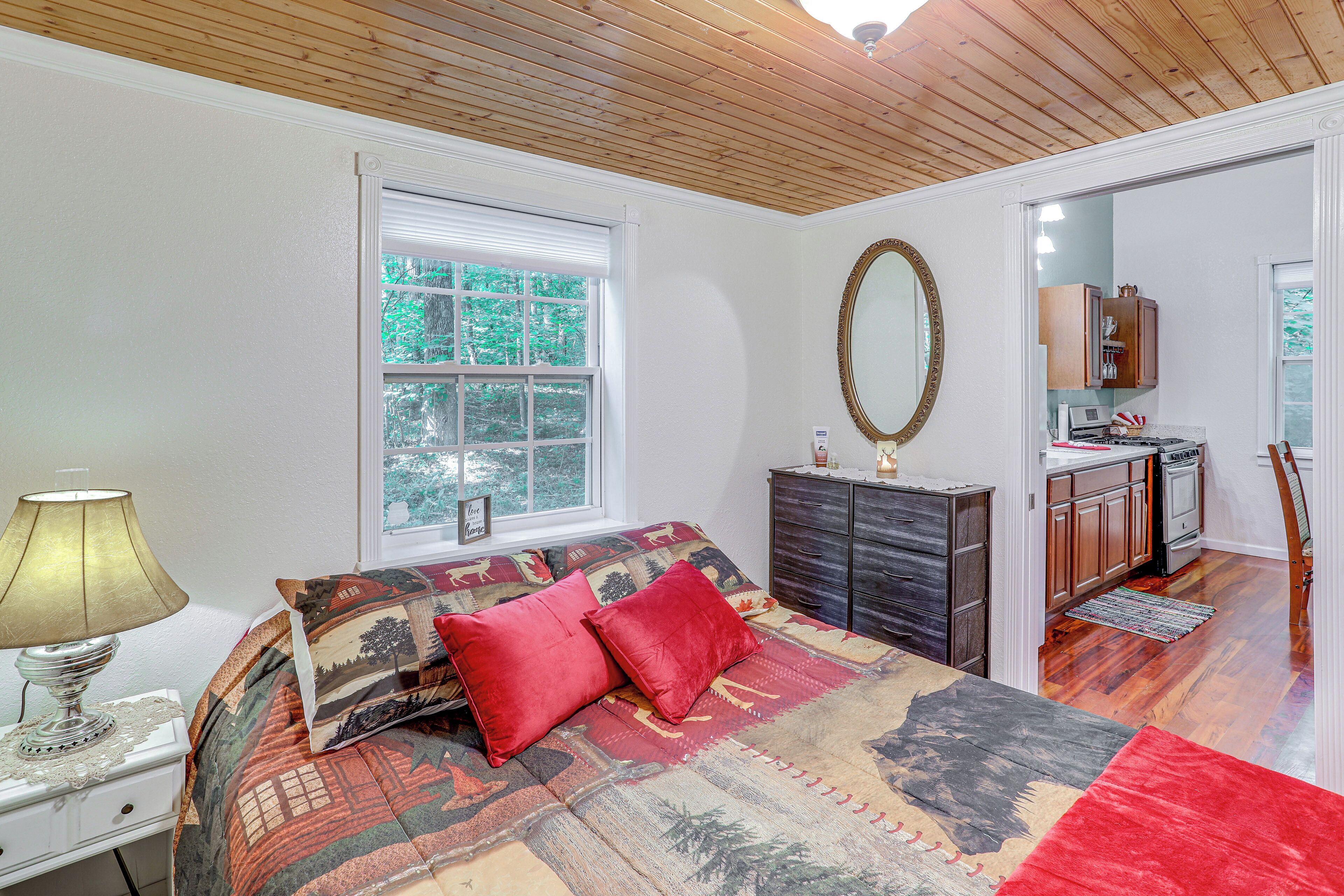 A bedroom with a large bed, a dresser, a mirror, and a window with a view of trees.